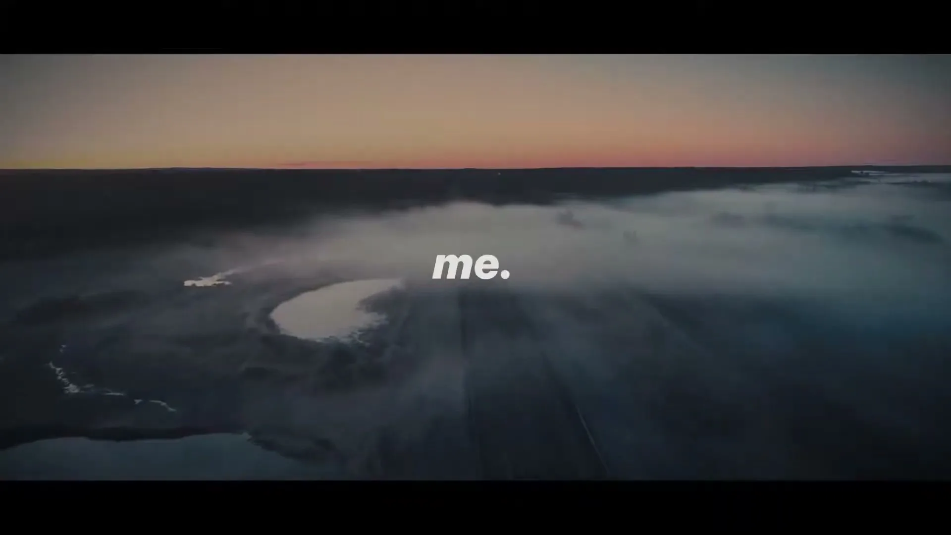 An aerial wide shot shows a misty landscape with a body of water and a road at dawn, with the text "to" and "me." appearing on screen.