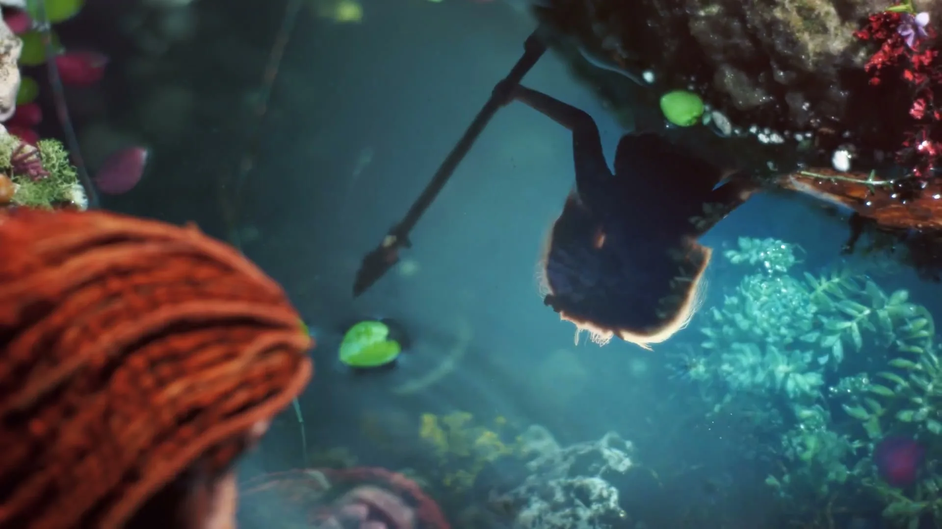 A person with red hair looks into a pond, seeing their reflection and the reflection of another person holding a spear.