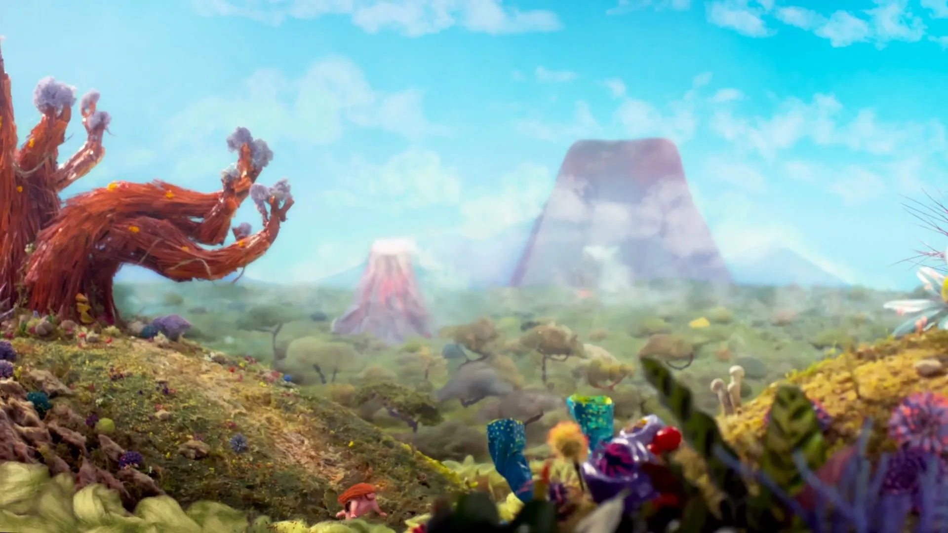Two small, stylized human figures are seen on a hill next to a large, red, gnarled tree, looking out over a fantastical landscape with distant mountains and volcanoes under a blue sky.