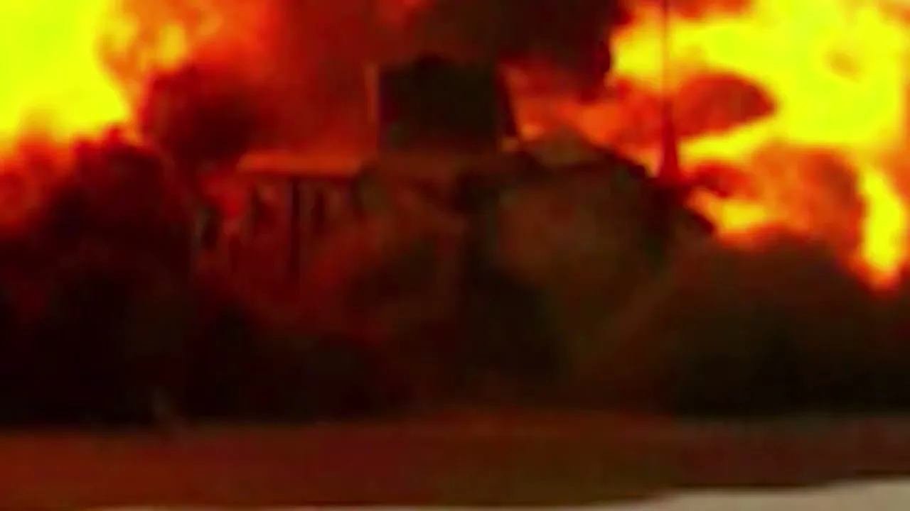 A military vehicle is parked on a dusty street, then a massive explosion erupts behind it, engulfing the scene in fire and smoke.