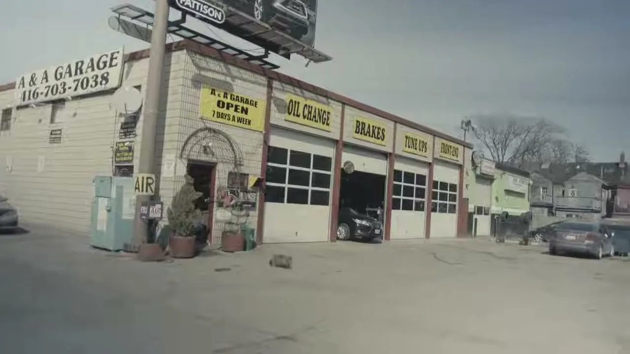 A wide shot of a grey garage with multiple bays and a billboard on top, with cars parked outside on a clear day.