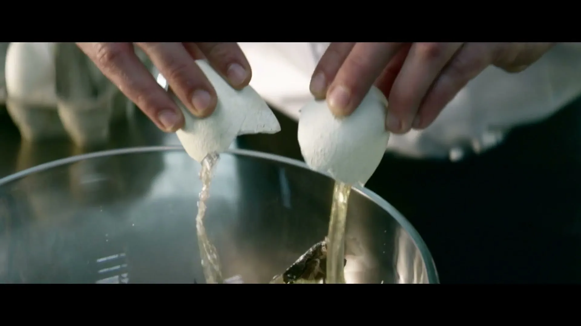 A chef's hands crack an egg into a glass bowl, revealing a small dinosaur inside, in a kitchen.