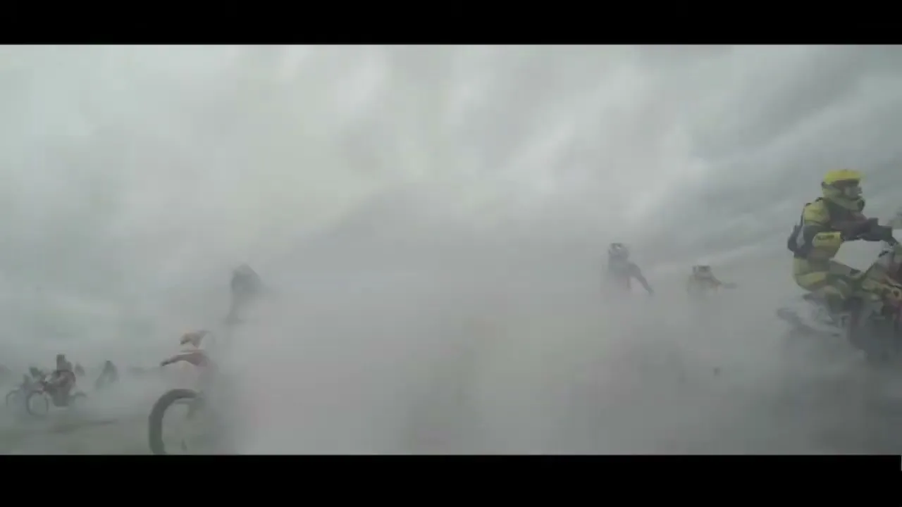 Several motocross riders on dirt bikes speed through a dusty, outdoor track under a cloudy sky.