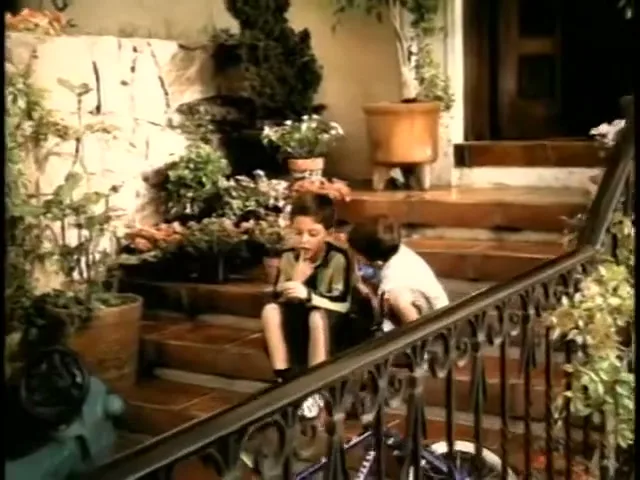 Two young boys sit on the front steps of a house, one boy examining something in his hand while the other looks on.