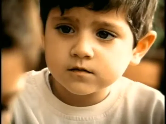 A young boy with dark hair and a white t-shirt looks intently at someone off-screen in a medium closeup shot.