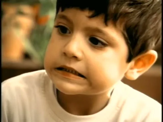 A young boy with dark hair and a white t-shirt looks off-camera with a slightly worried expression in an interior setting.