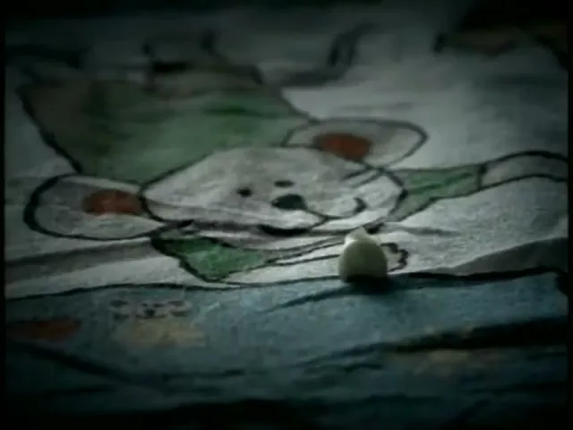 A small white tooth lies on a child's bedsheet with a cartoon mouse design, in a dimly lit room.