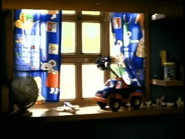 A toy truck and a globe sit on a window sill with blue curtains, as a hand quickly reaches in from the right to grab something.