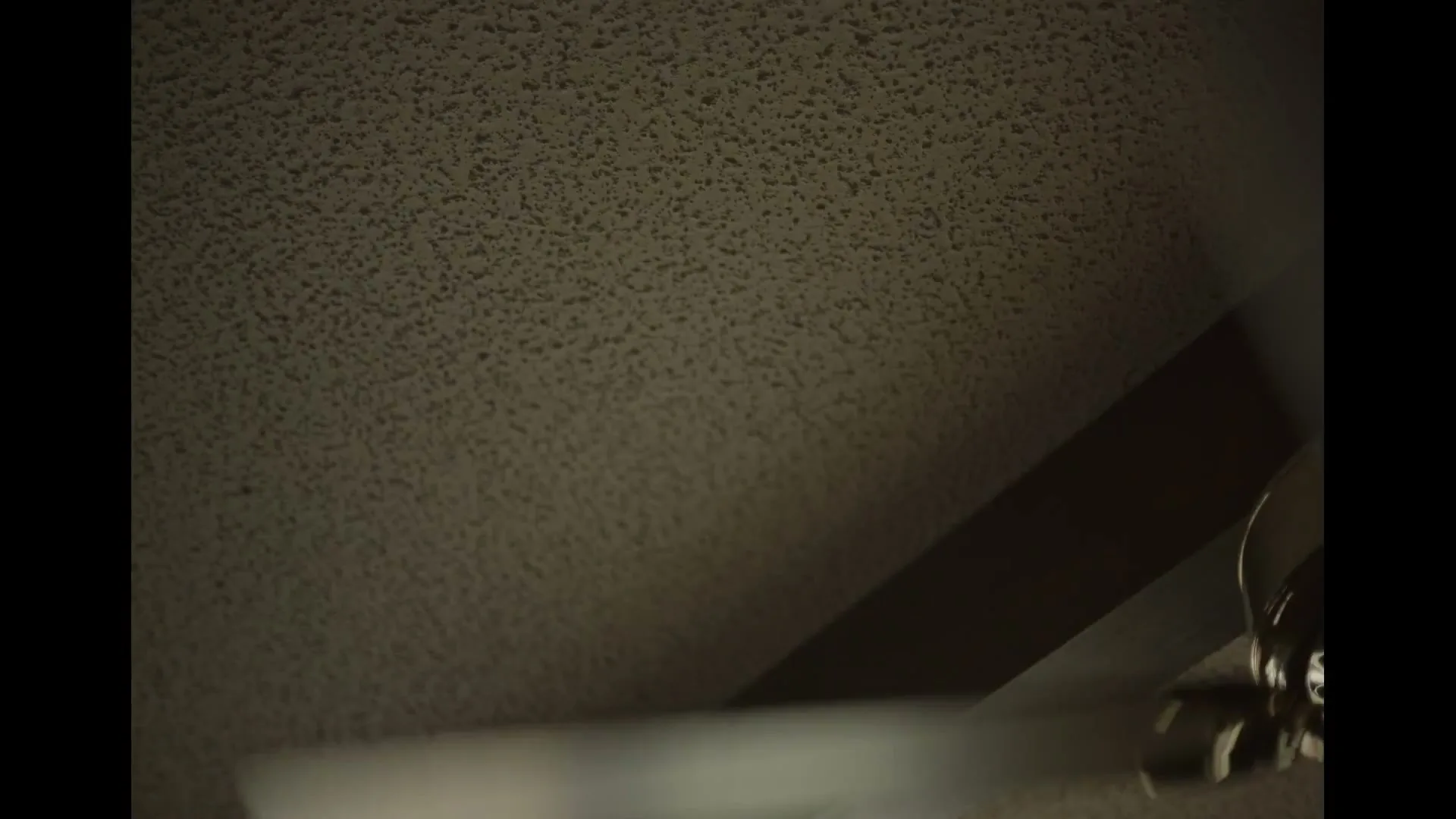 A low-angle shot of a white ceiling fan spinning rapidly against a textured, off-white ceiling, with a dark shadow cutting across the frame.