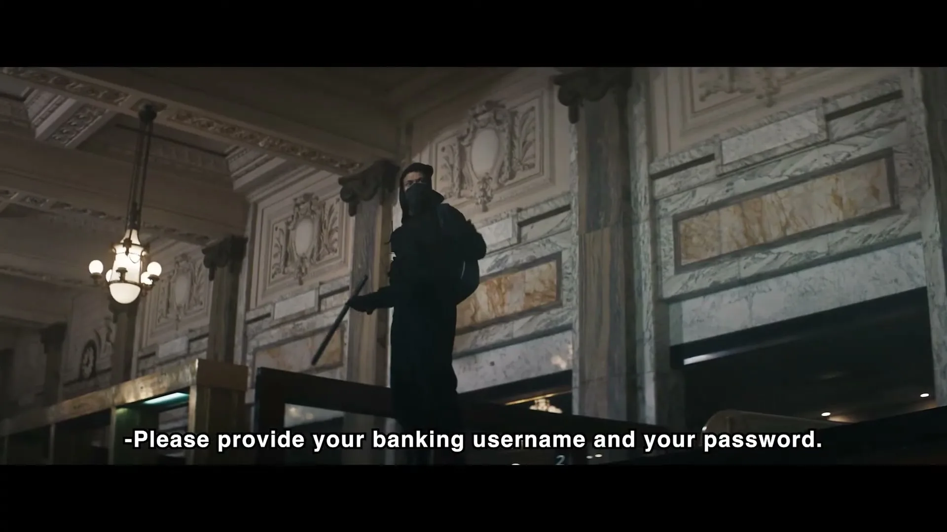 A person in a black hoodie and mask stands on a ledge inside a grand, ornate bank, holding a long stick.