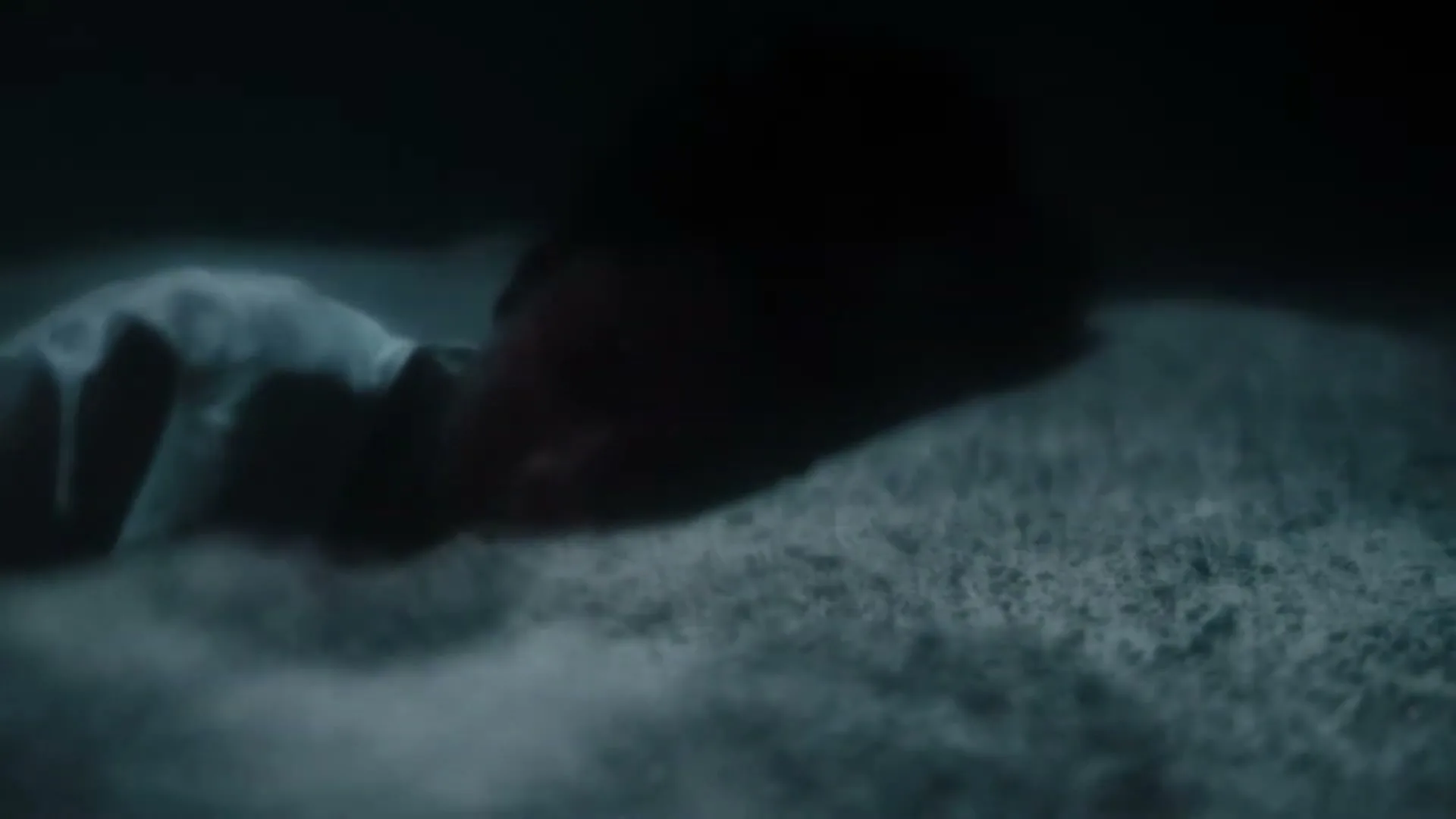 A person lies on a sandy surface in the dark, their face obscured, with a hand visible in the foreground.