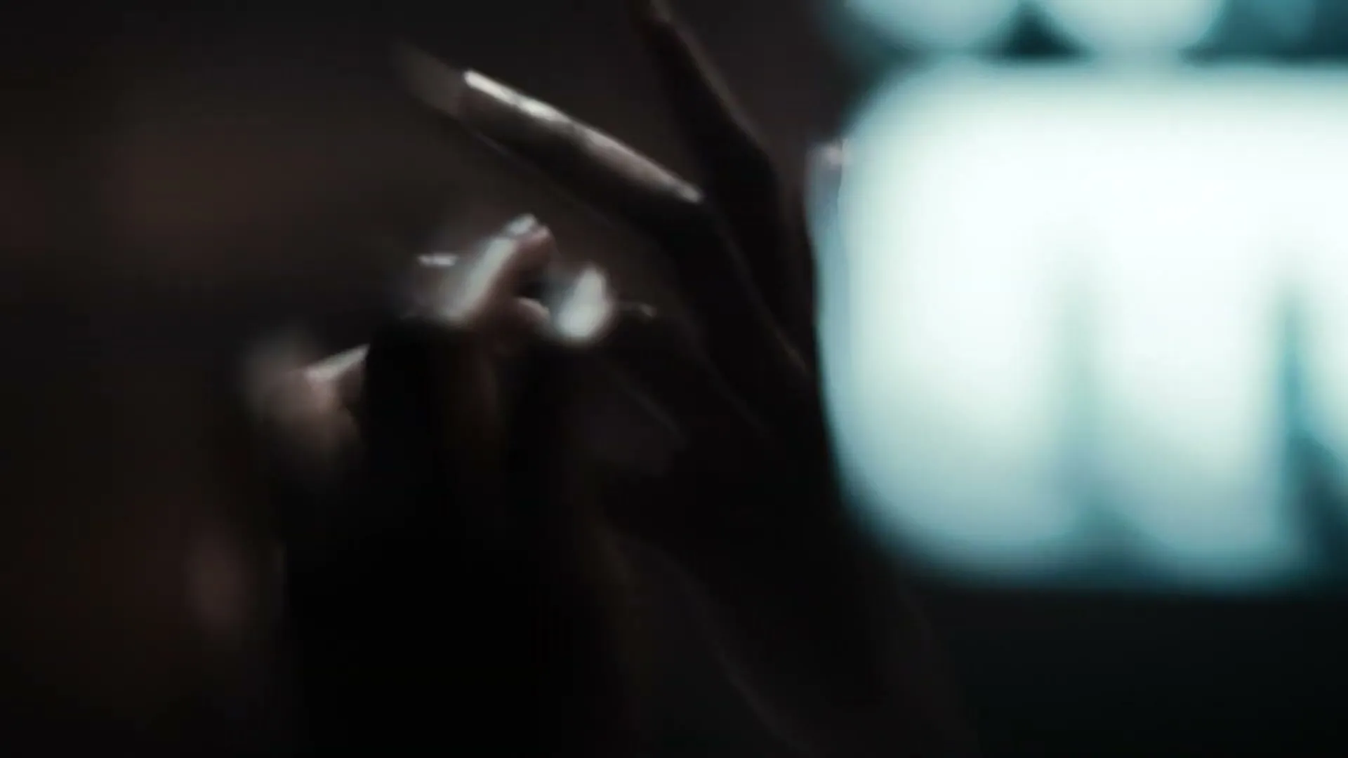 A person's hands are shown in a blurry, dark shot, with a bright, out-of-focus light source in the background.