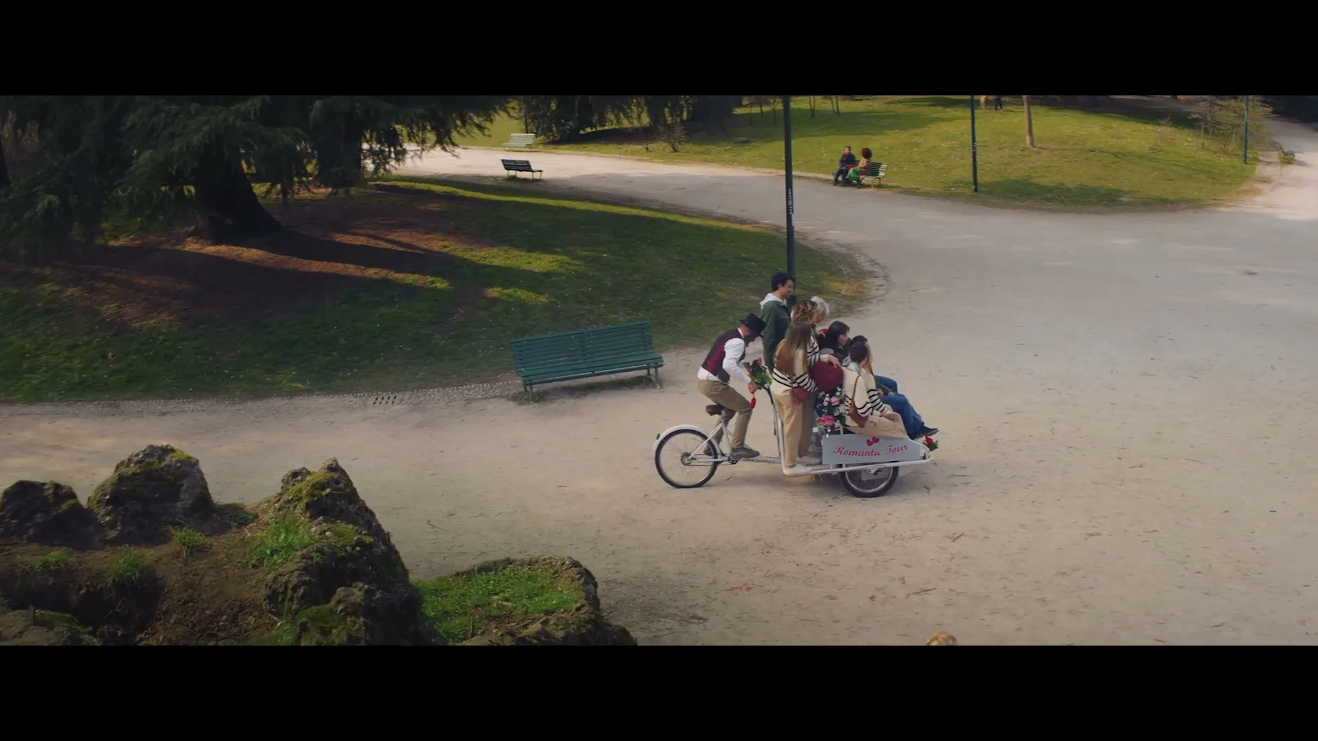 A group of young adults with Down Syndrome ride a tandem bicycle with a carriage through a sunny park, enjoying the day.