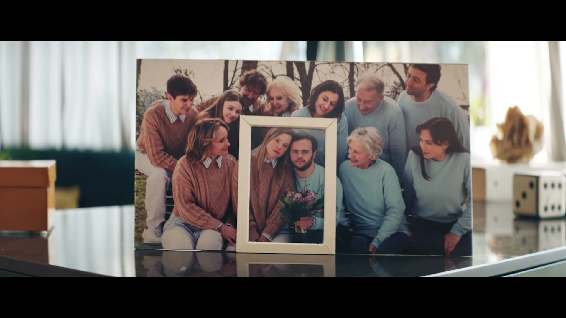 A framed photo of a large family, with a smaller framed photo of a couple with Down Syndrome nested inside, sits on a reflective surface in a bright room.
