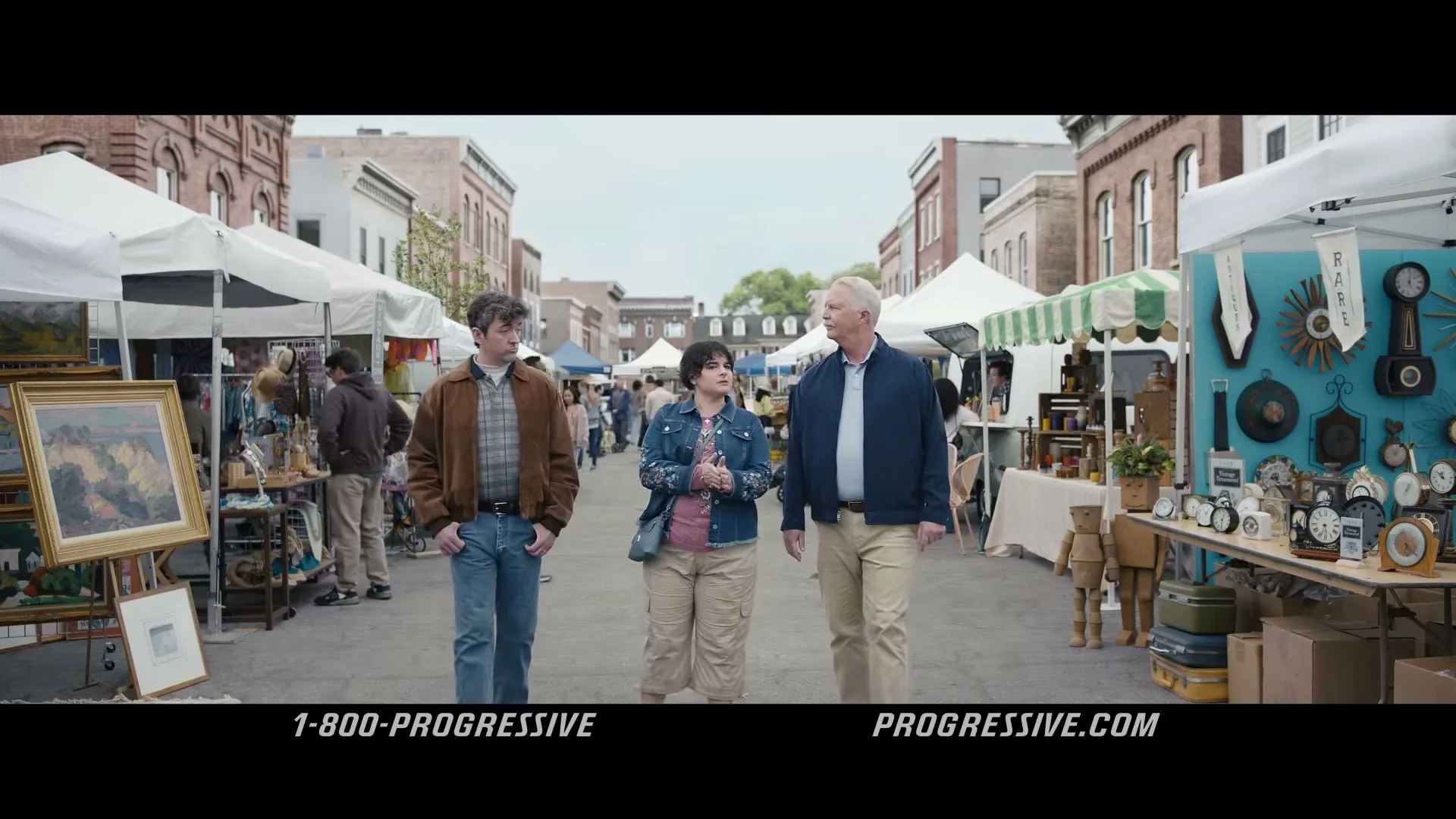 Dr. Rick walks with a young couple through an outdoor market, looking at various stalls and items.