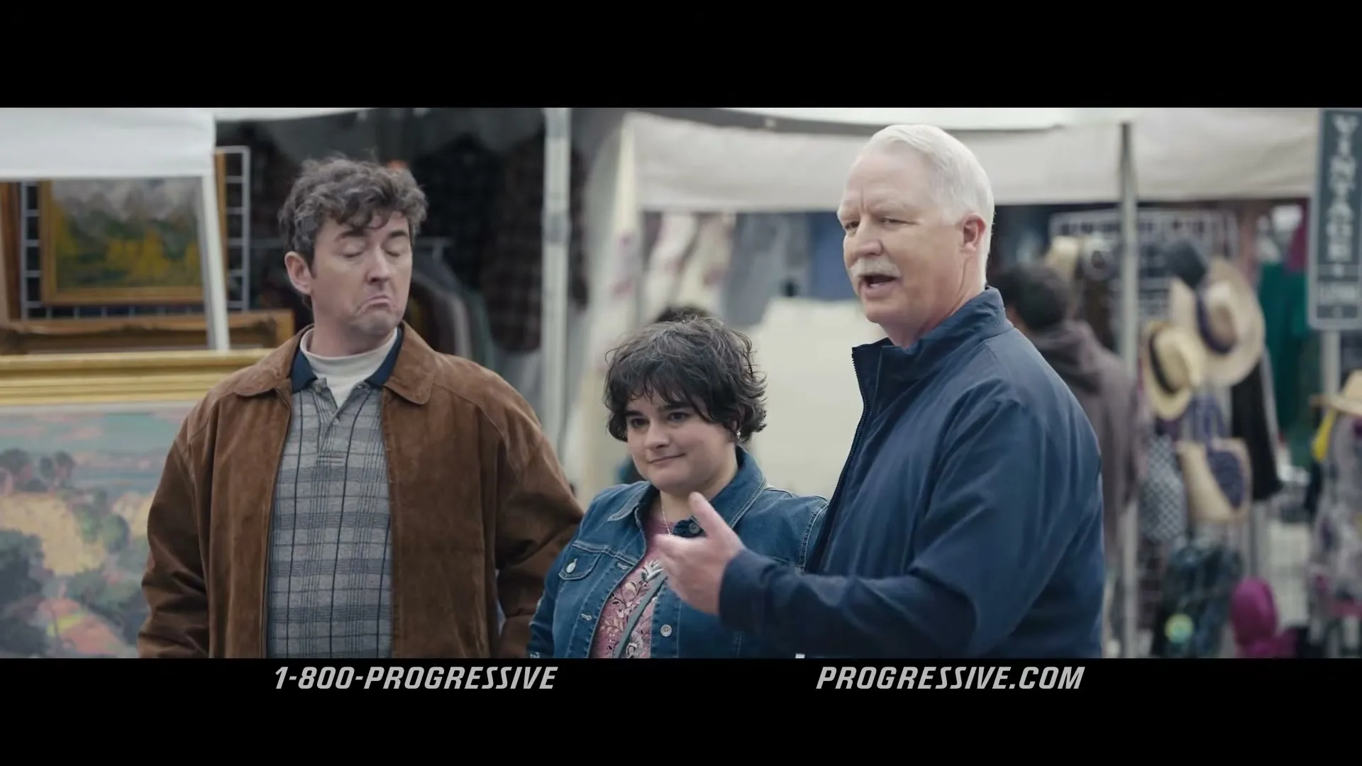 Dr. Rick, a man in his 60s, talks to a young couple at an outdoor market, while the man looks confused.