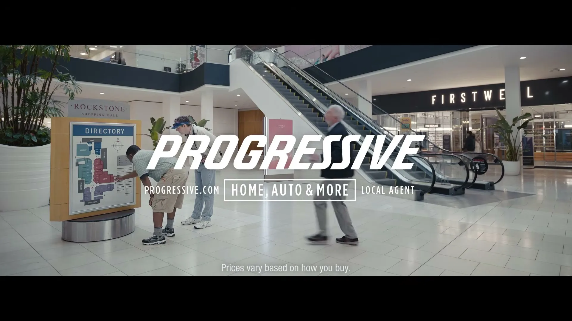 Two men look at a directory in a bright, modern shopping mall, while an older man walks past them.