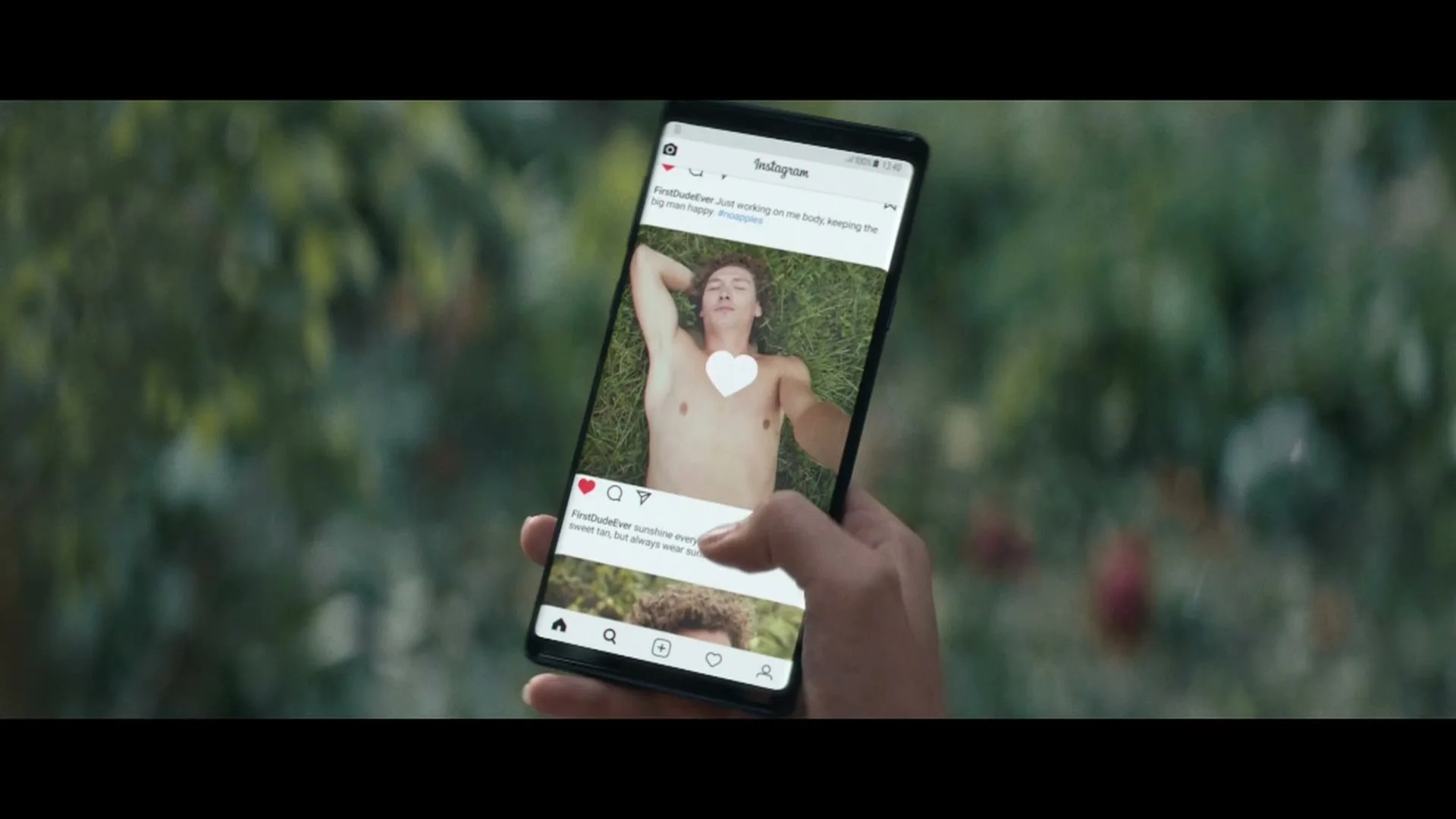 A hand holds a smartphone displaying an Instagram feed with shirtless photos of a man with curly hair, as the user scrolls through the posts outdoors.
