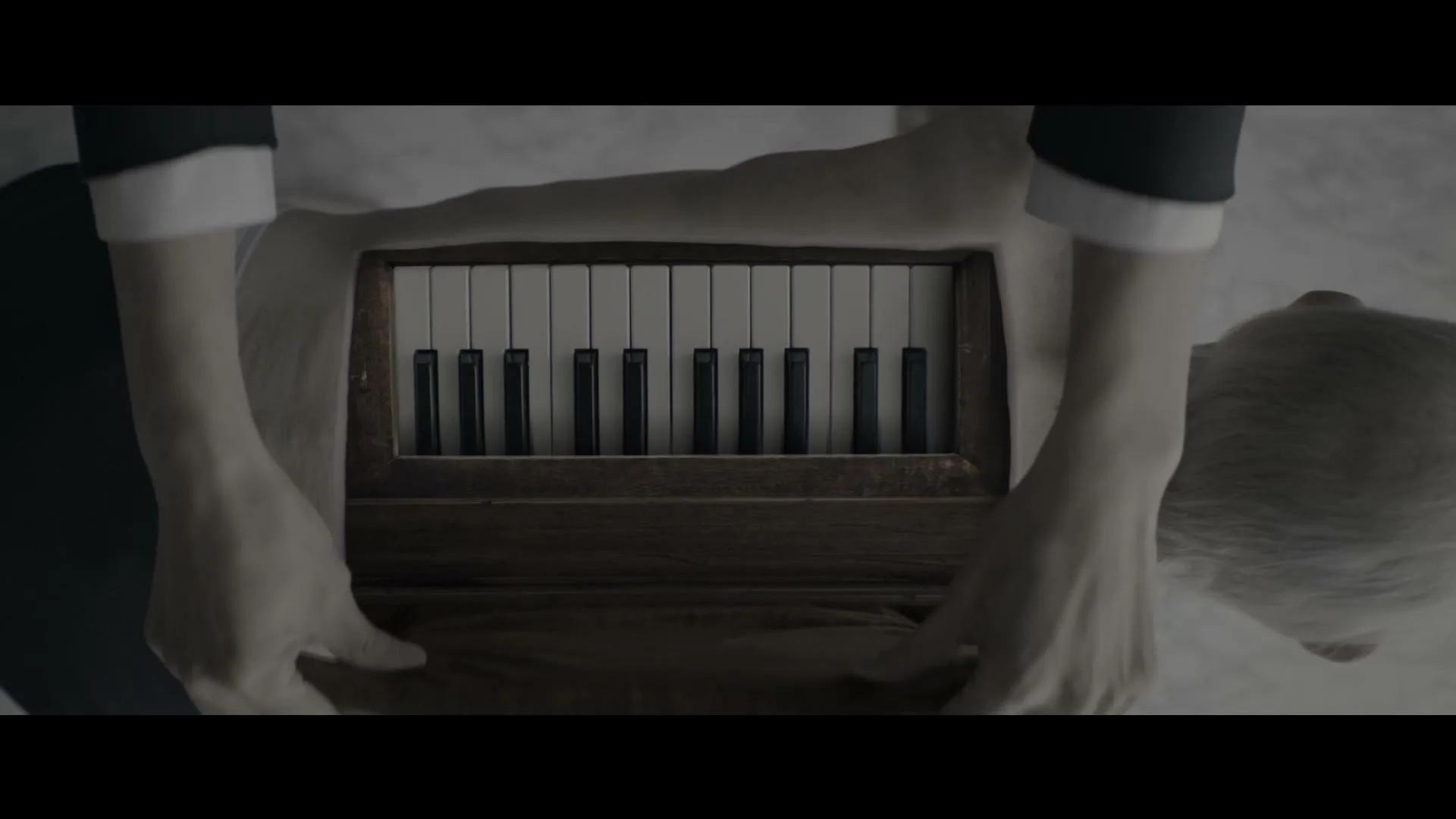 A person's back is shown with a piano keyboard embedded, as hands appear to be playing it, in a surreal, dimly lit setting.