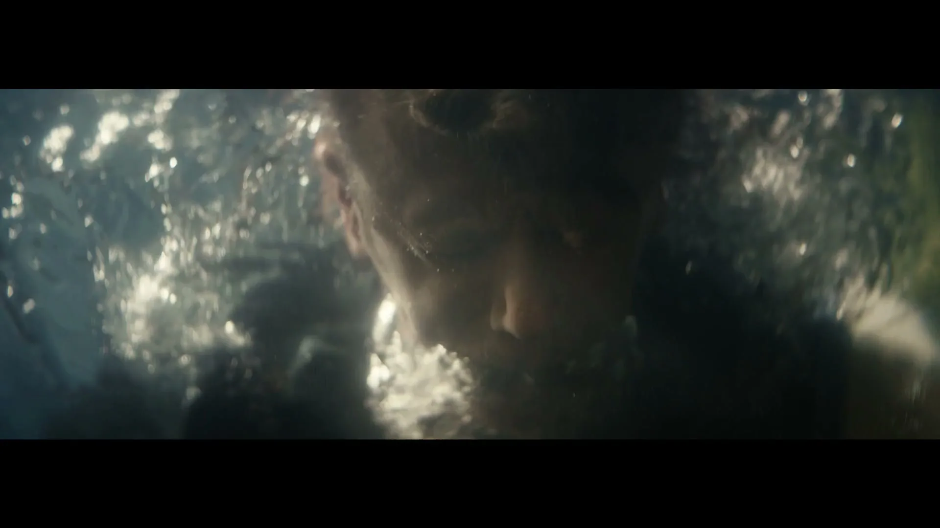 A person is submerged underwater, struggling as bubbles escape their mouth, with light filtering through the disturbed surface.