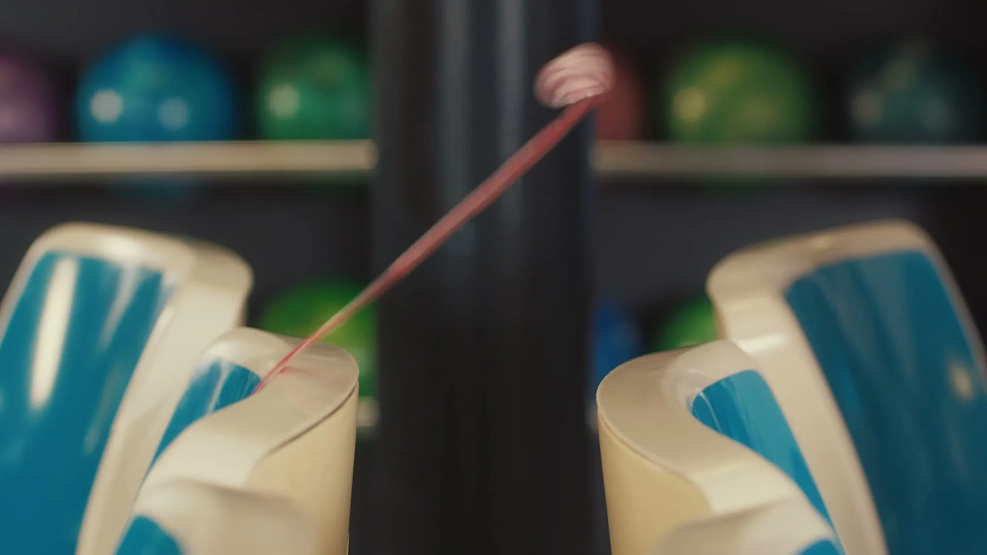A red Fruit by the Foot candy is stretched between two bowling ball return slots in a bowling alley.