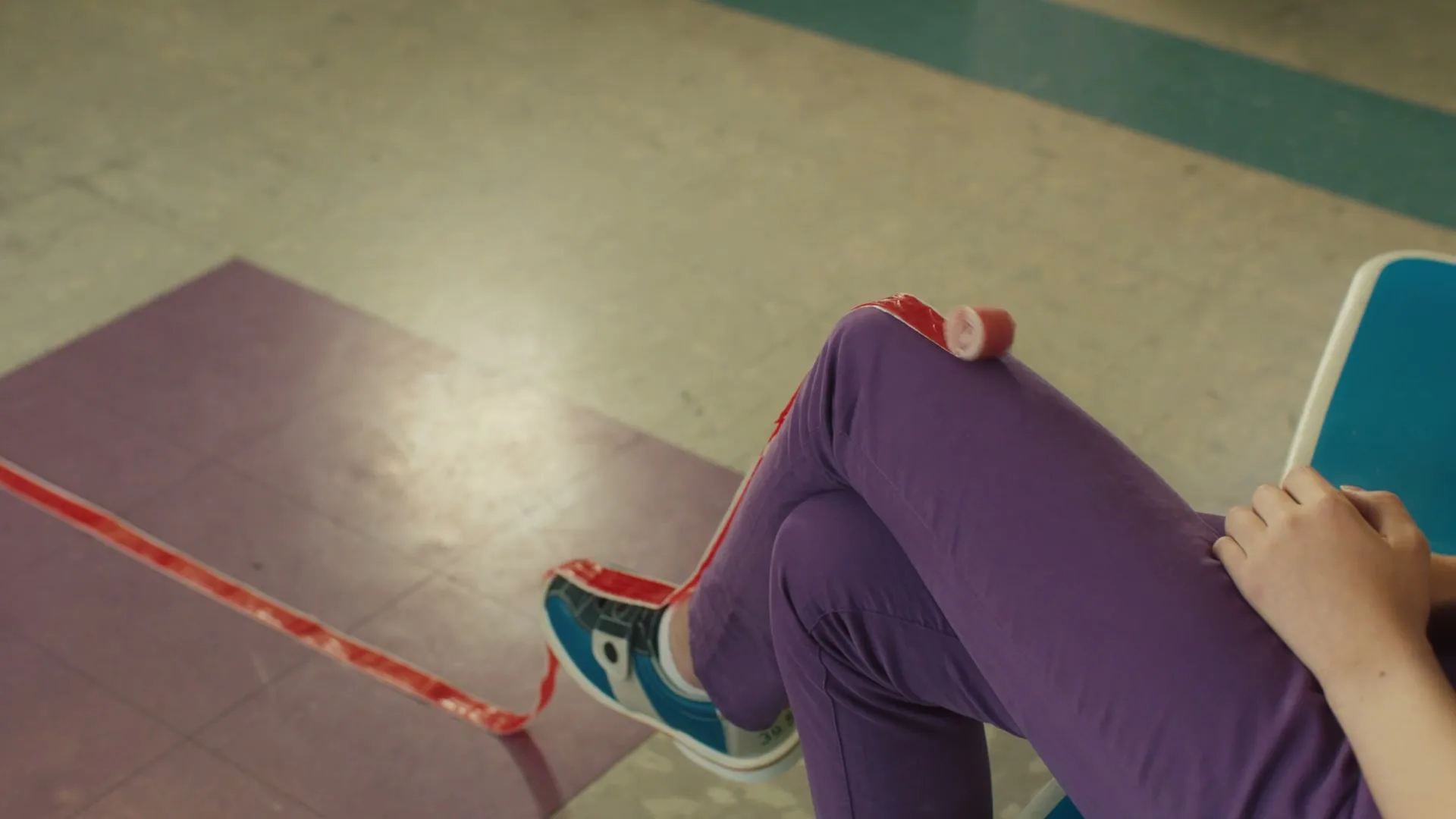 A person in purple pants and blue shoes sits with a Fruit by the Foot unrolling from their lap onto the floor.