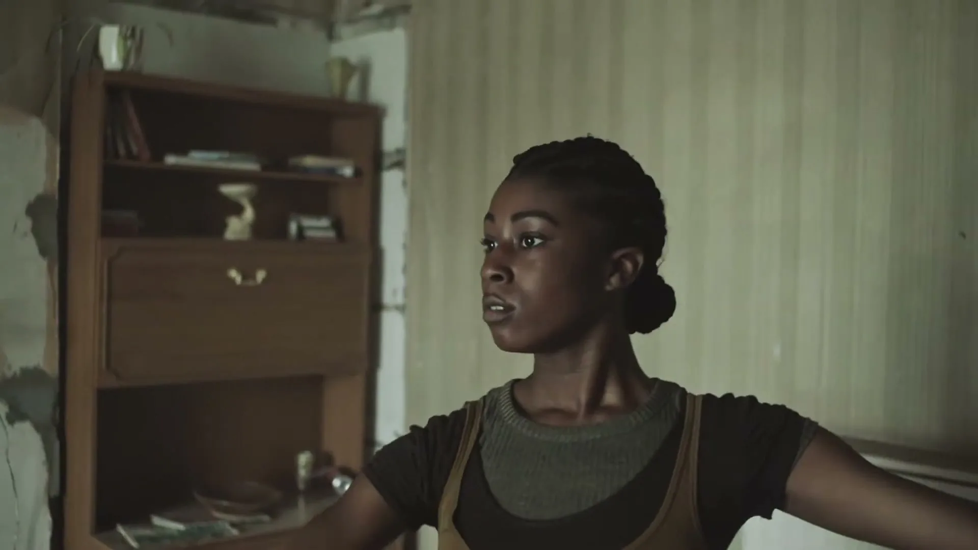 A young Black woman with braided hair practices ballet in a dilapidated room, looking focused and determined.