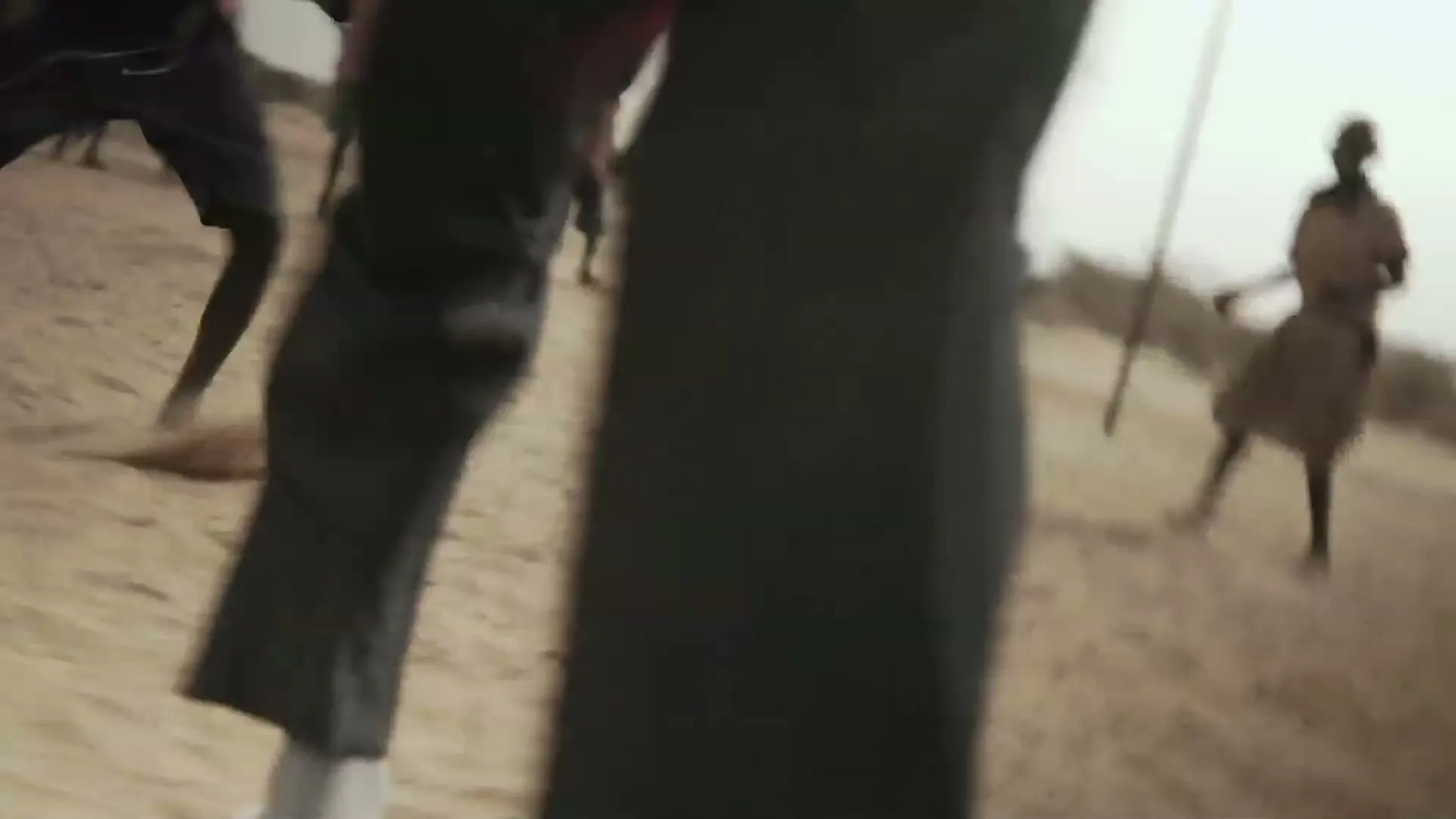 A group of children play soccer on a dusty field, with one child in a red hoodie running towards the camera.