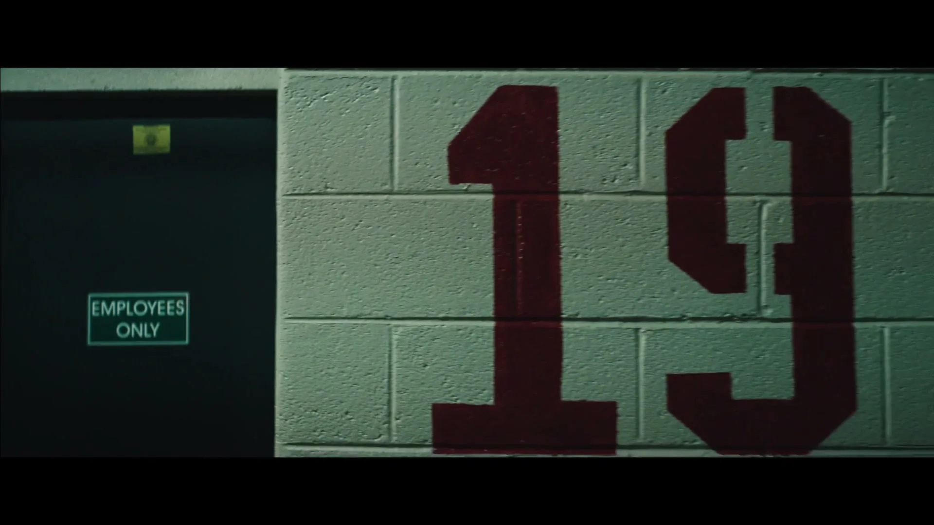 A dark door with an "Employees Only" sign is next to a white brick wall with the number "19" painted in red.