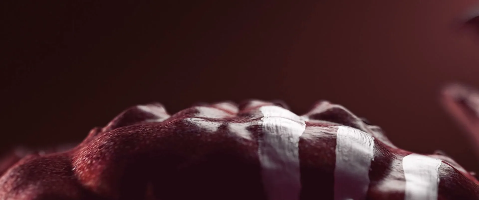 A macro shot of a red, textured surface with white stripes, resembling a creature's skin, against a dark red background.