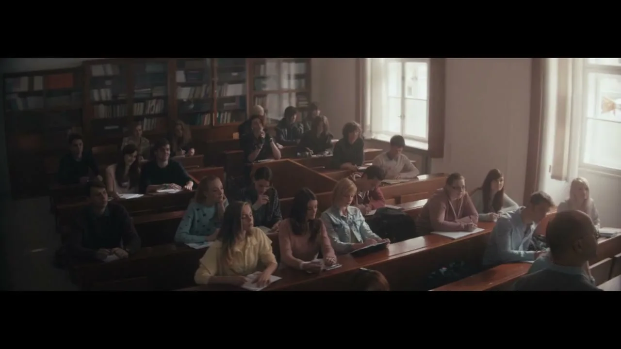 A diverse group of students sits in a sunlit classroom, listening attentively to a lecture.