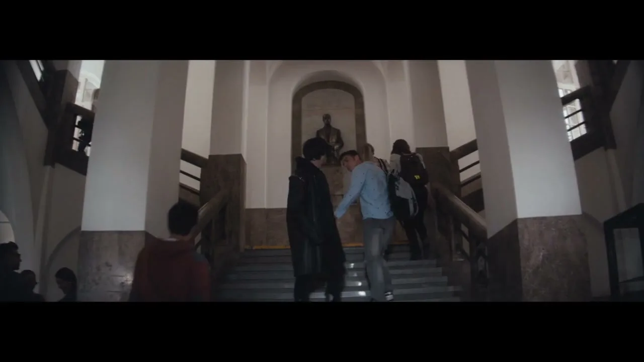 A group of students walk up a grand staircase in a school building, with one student looking back at another.