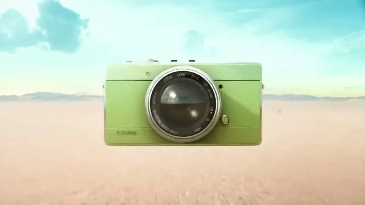 A green camera floats in a desert landscape, then the camera lens opens to reveal the inner workings of the camera.
