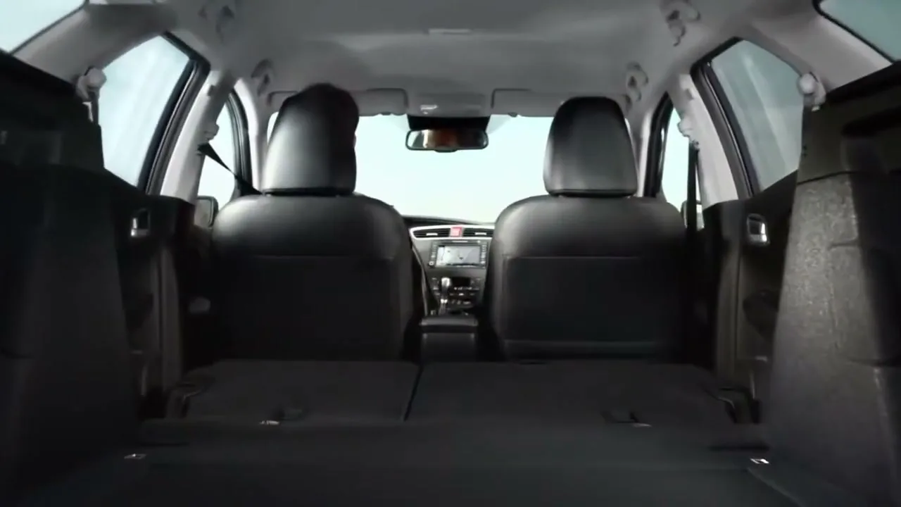 The camera moves from a dark, abstract view to reveal the interior of a car's trunk with the back seats folded down, showing the front seats and dashboard.