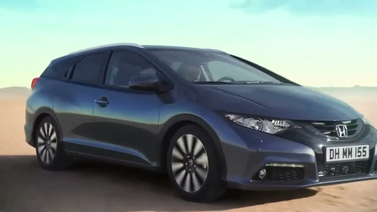 A dark grey Honda Civic car drives on a dirt road in a desert landscape under a clear sky.