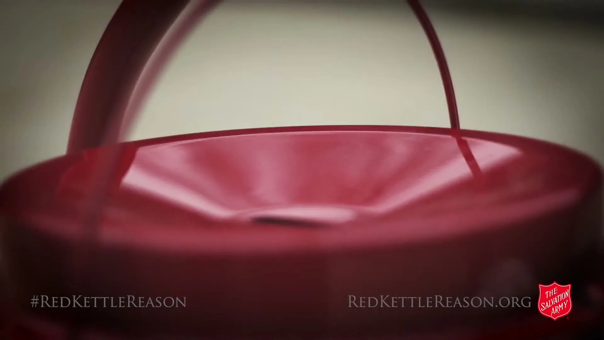 A close-up shot of a red Salvation Army kettle, with the top of the kettle and its handle visible, against a blurred light background.