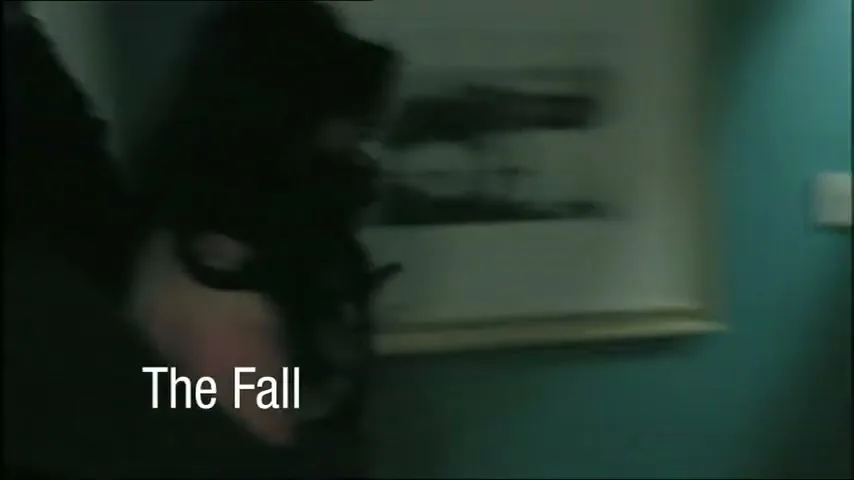 A woman with dark hair and a gag over her mouth is seen in a dark room, struggling against an unseen force.