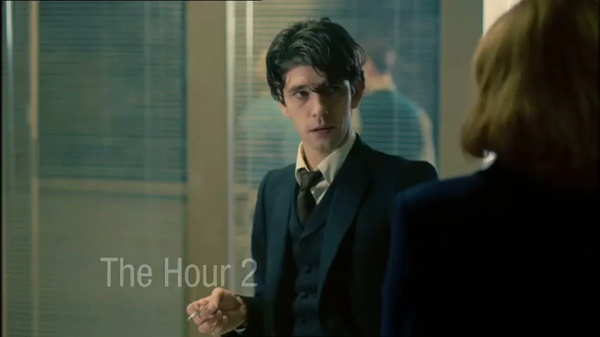 A young man in a suit holds a cigarette and looks at a woman's back in an office, with "The Hour 2" text on screen.