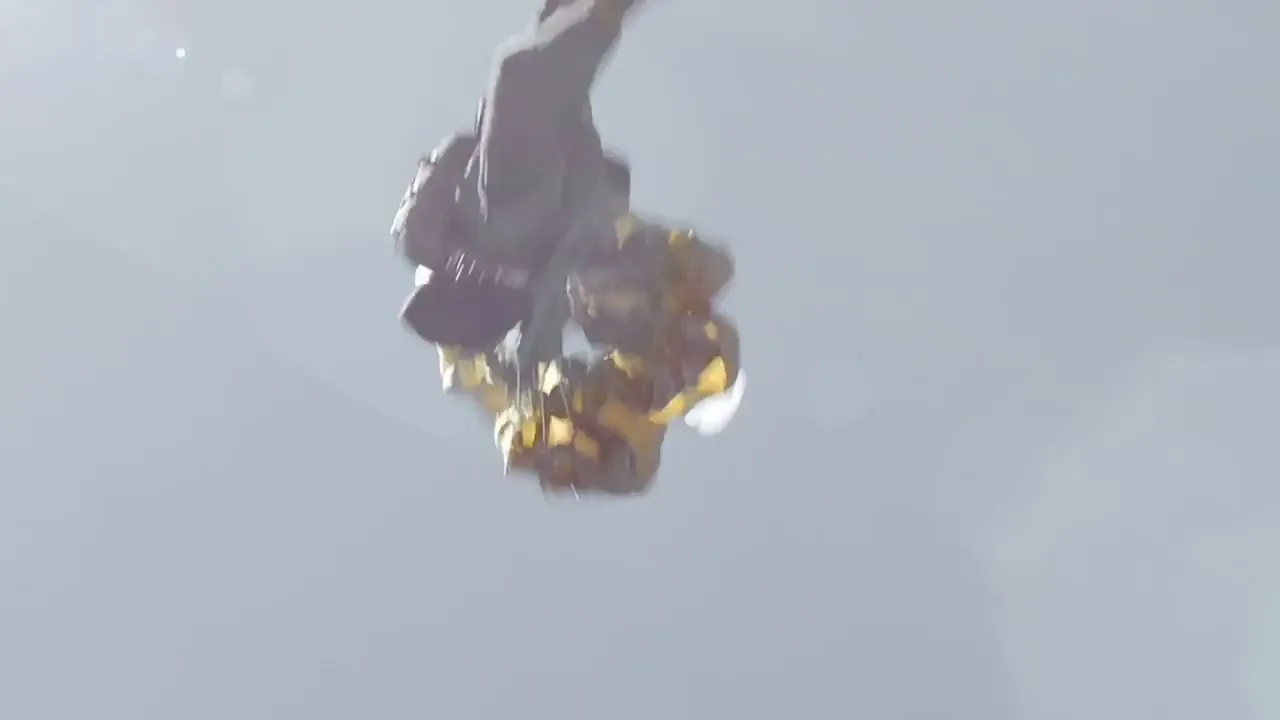 A person in a dark suit and a yellow parachute is seen falling through the sky, with the sun shining brightly in the background.