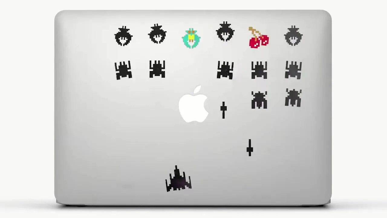 A MacBook Pro with various stickers on its lid, including Catwoman, Space Invaders, and scuba divers, against a white background.