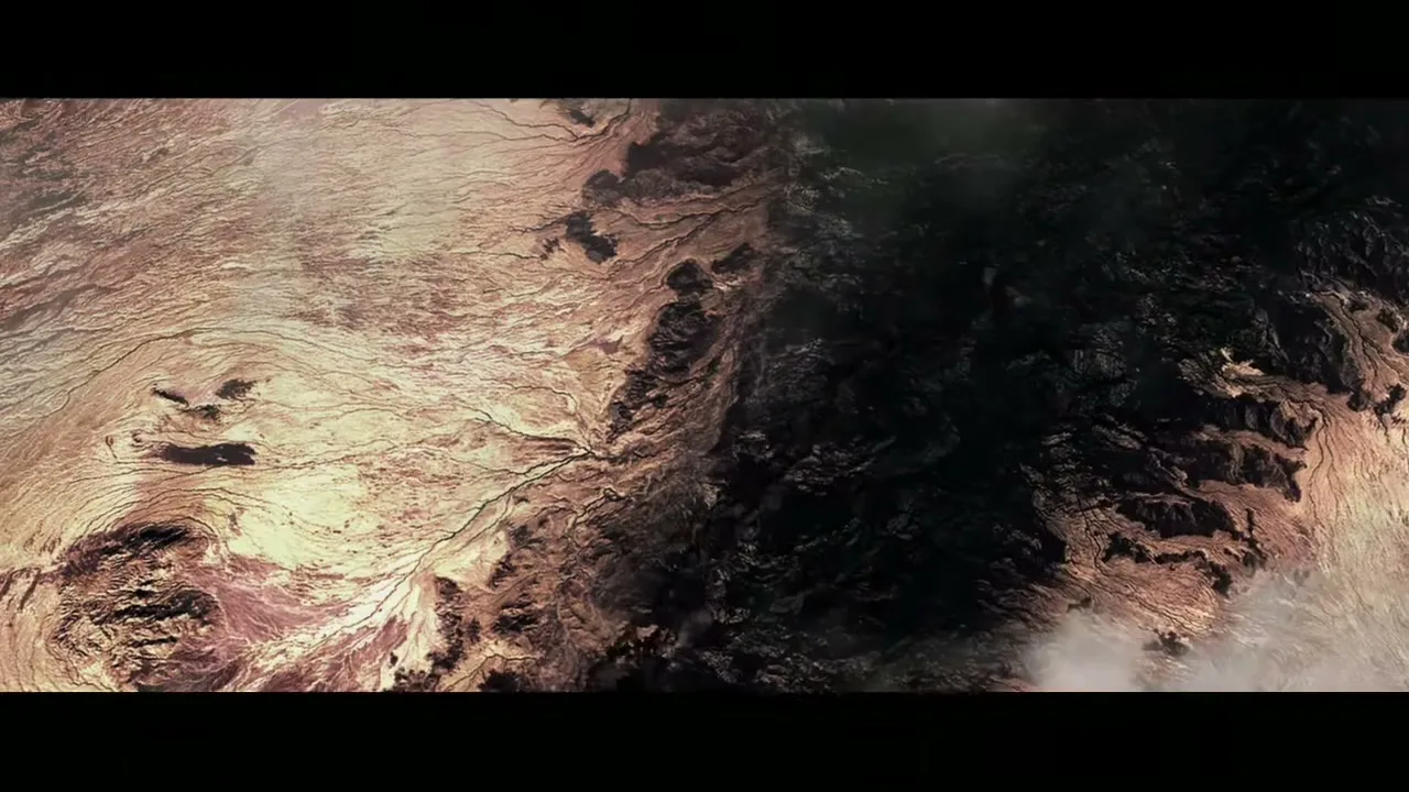An extreme wide shot from above shows a vast, dark, and rugged landscape with some lighter, sandy areas, as if seen from space.