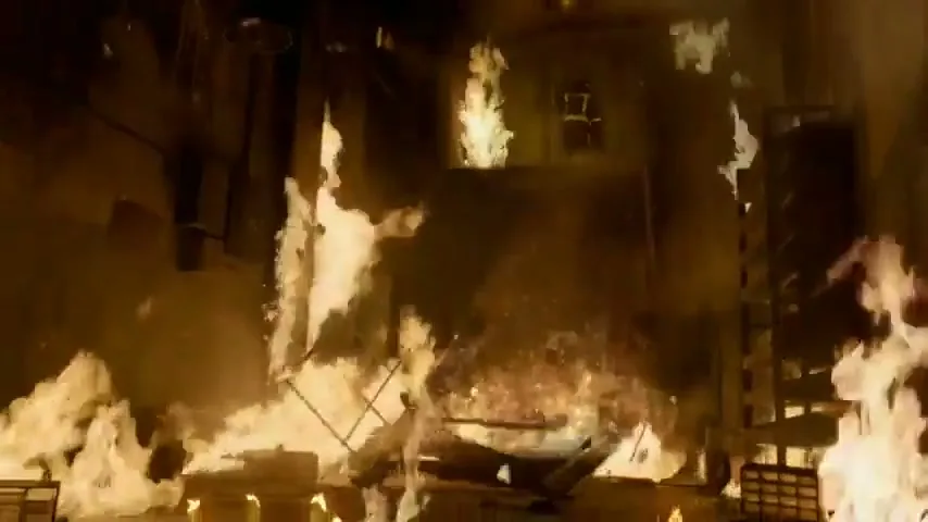 A wide shot shows a room engulfed in flames, with debris falling and fire spreading rapidly.
