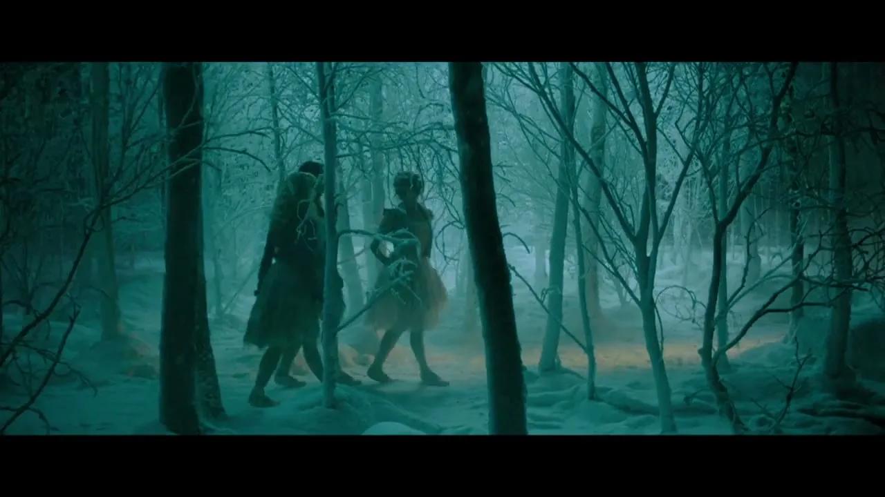 Two women in period costumes walk through a dark, snowy forest, with one woman holding a small dog on a leash.