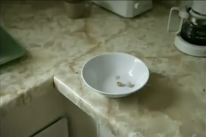A white bowl with small green objects in it sits on a marble countertop in a kitchen.