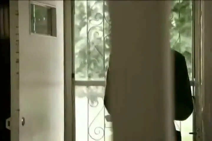 A young man in a red shirt and green cardigan walks into a house, holding a carton of milk, with a dog visible outside the screen door.