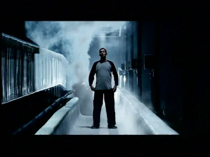 A man stands in a dark, icy bobsled track with steam rising around him, looking determined.