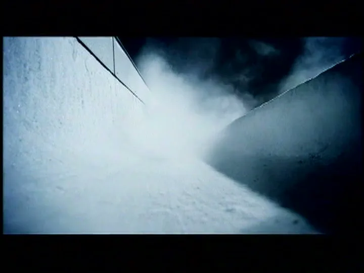 A bobsled speeds down an icy track, kicking up a cloud of snow and ice as it rounds a corner at high speed.