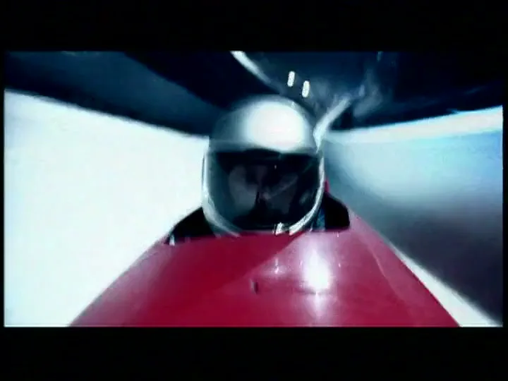A bobsledder in a helmet speeds down an icy track at night, with the camera mounted on the bobsled.