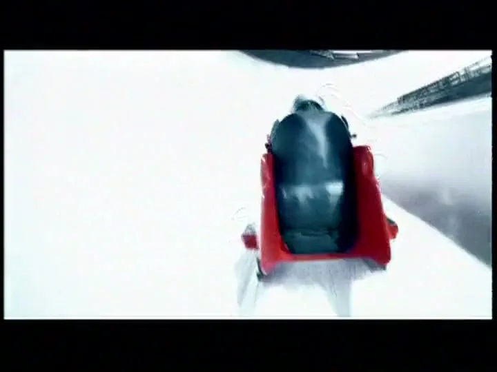 A bobsled with a person inside speeds down a track, transitioning from a dark, lit track to a bright, white, abstract environment.