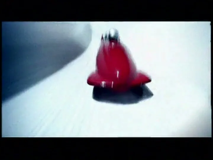 A red bobsled with a silver helmeted person inside speeds down an icy track, with the camera following closely.